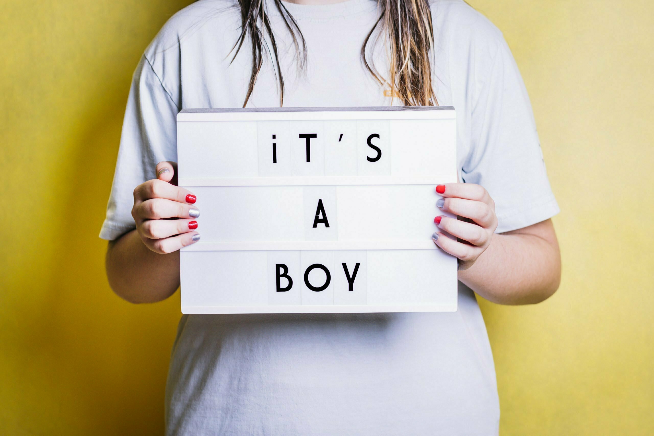 Girl holding a light box with the phrase "it's a boy".